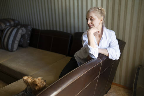 Frau sitzt auf dem Sofa und schaut auf einen Yorkshire Terrier - TETF02335