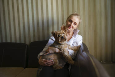 Porträt einer Frau, die einen Yorkshire-Terrier im Wohnzimmer hält - TETF02337
