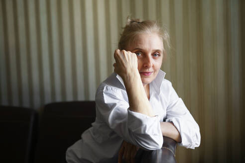 Porträt einer Frau, die sich auf die Rückenlehne eines Sofas stützt und in die Kamera schaut - TETF02338