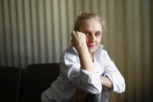 Portrait of woman leaning on sofa backrest and looking at camera - TETF02338