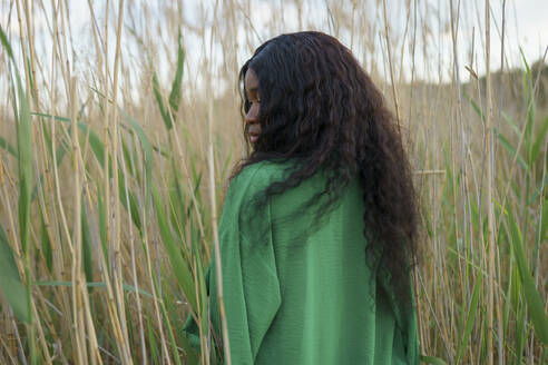 Brunette woman standing among long grass in field - TETF02343