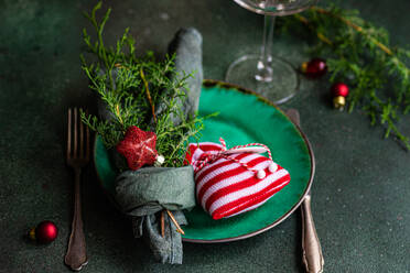 Weihnachtssäckchen und Tannenzweige, eingewickelt in ein Taschentuch, auf einem Teller, der auf einem grünen Tisch neben Glas und Gabeln steht - ADSF47870