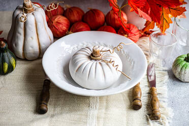 High angle of autumnal table setting with white pumpkin on plate placed on table near cutlery, glasses and red onions and leaves - ADSF47887