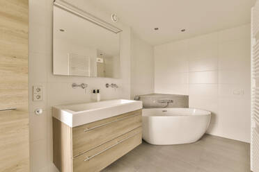 Interieur eines modernen Badezimmers mit stilvoller Badewanne und Spiegel über dem Waschbecken, umgeben von gefliesten Wänden und Böden - ADSF47961