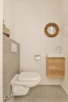 Interieur eines modernen Badezimmers mit Toilettenschüssel und Spiegel über dem Waschbecken mit Holzschrank an einer weißen Wand in einer modernen Wohnung - ADSF47965