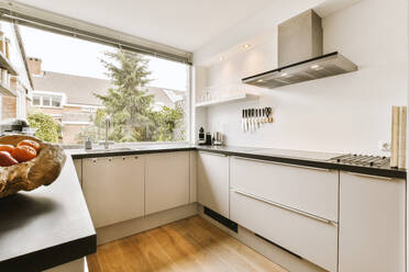 Innenansicht einer geräumigen Küche mit weißen Schränken und schwarzer Arbeitsplatte neben einem großen offenen Fenster in einer modernen Wohnung - ADSF47976