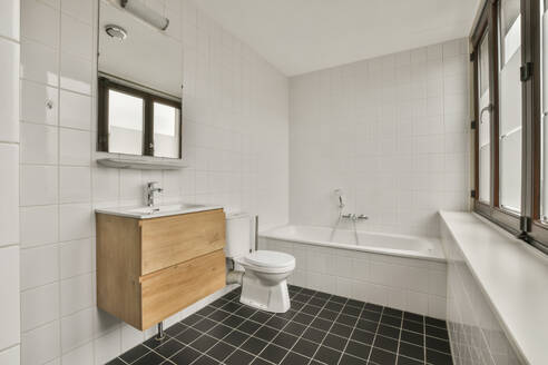 Innenraum eines privaten Badezimmers mit Badewanne und Toilettenbecken neben einem Keramikwaschbecken in einem modernen Haus - ADSF47984