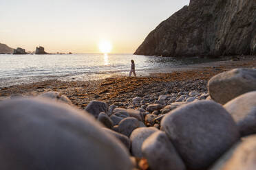 Ältere Frau geht bei Sonnenuntergang am Meer spazieren - MMPF00937