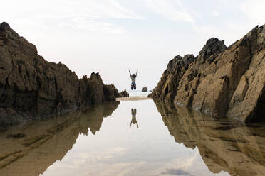 Woman jumping near water puddle under sky - MMPF00949