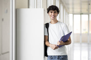 Lächelnde Schülerin mit Aktenordner im Korridor - LMCF00602