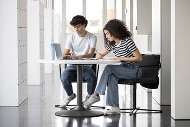 Studentin mit Laptop und Freund beim Schreiben am Tisch in der Universität - LMCF00616