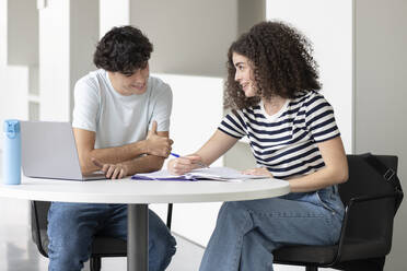 Smiling student explaining friend at table in university - LMCF00622