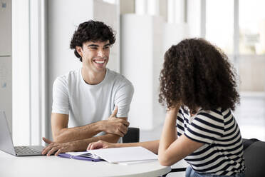 Lächelnde Studenten, die sich am Tisch in der Universität unterhalten - LMCF00624