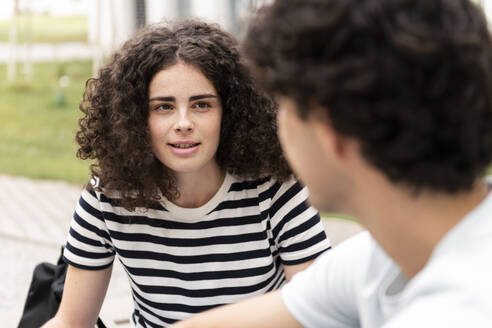 Lächelnder Student im Gespräch mit einem Freund auf dem Campus - LMCF00634