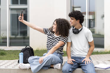 Glückliche Studenten posieren vor Gebäude und halten in einem Selfie ihre Freude fest - LMCF00641