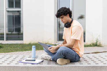 Junge Studentin mit Laptop auf einer Betonbank auf dem Campus - LMCF00645