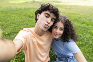 Smiling couple with puckering face taking selfie on grass in park - LMCF00661