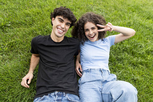 Smiling friend with woman gesturing peace sign on grass - LMCF00664