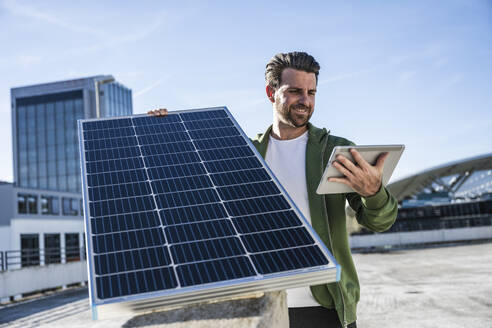 Engineer holding digital tablet and solar panel on sunny day - UUF30532