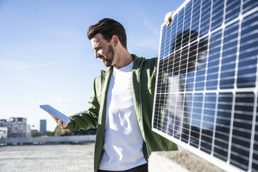 Ingenieur schaut auf ein digitales Tablet und hält ein Solarpanel an einem sonnigen Tag - UUF30537