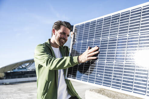 Smiling engineer analyzing solar panel on sunny day - UUF30542