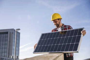 Ingenieur mit Schutzhelm bei der Prüfung eines Solarpanels - UUF30543