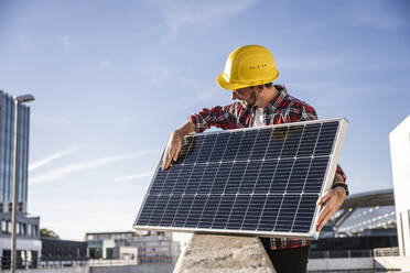 Ingenieur mit Schutzhelm bei der Analyse eines Solarpanels an einem sonnigen Tag - UUF30547