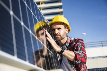 Selbstbewusster Ingenieur mit Schutzhelm bei der Prüfung eines Solarpanels - UUF30548