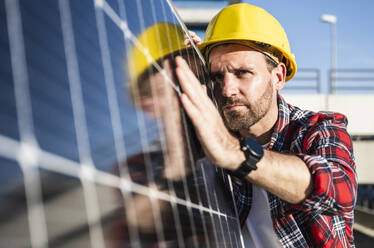 Selbstbewusster Ingenieur mit Schutzhelm bei der Analyse eines Solarpanels - UUF30549