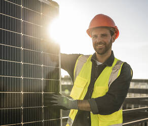 Lächelnder Ingenieur vor einem beleuchteten Sonnenkollektor auf der Terrasse - UUF30575