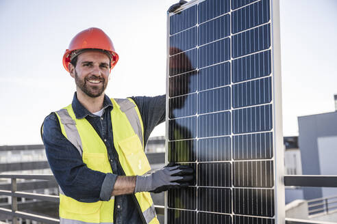Smiling engineer standing by solar panel at terrace - UUF30576