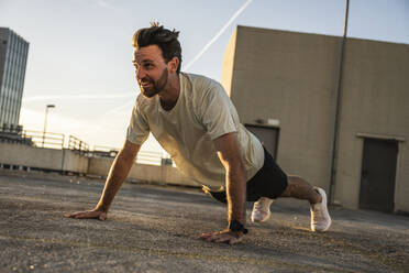 Active man doing push-ups on building terrace at sunset - UUF30586