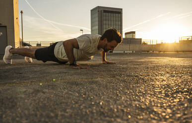 Active man doing push-ups on terrace at sunset - UUF30588