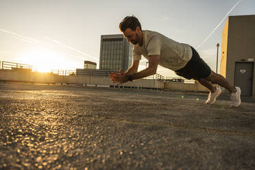 Active man doing push-ups on building terrace at sunset - UUF30589