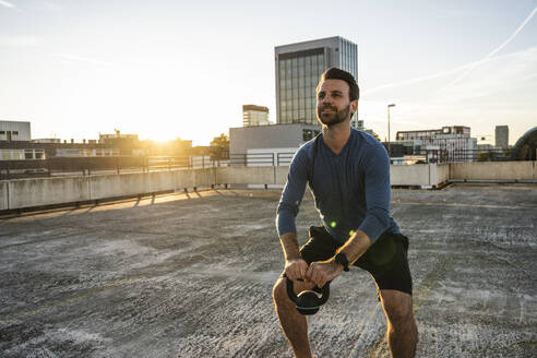 Aktiver Mann beim Training mit Kettlebell auf der Terrasse - UUF30590