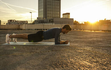 Mann übt Plankenstellung auf Terrasse bei Sonnenuntergang - UUF30597