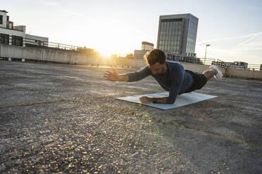 Aktiver Mann beim Üben der Plank-Position auf einer Matte bei Sonnenuntergang - UUF30598