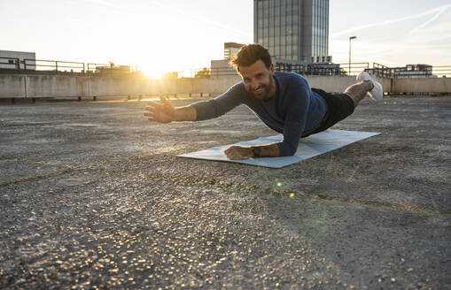 Lächelnder aktiver Mann, der bei Sonnenuntergang auf einer Matte die Plank-Position übt - UUF30600