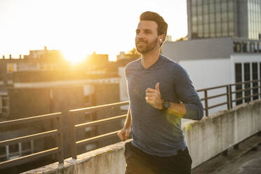 Active man running by railing on terrace at sunset - UUF30603