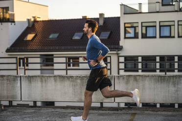 Active man jogging on terrace at sunset - UUF30605