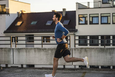 Aktiver Mann joggt bei Sonnenuntergang auf der Terrasse - UUF30605