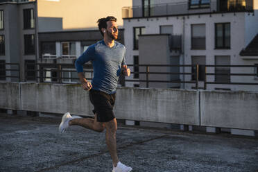 Active man running near railing on terrace at sunset - UUF30606