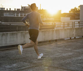 Active man jogging by railing on terrace at sunset - UUF30608