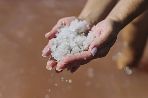 Hands of woman holding salt over lake water - SIF00913