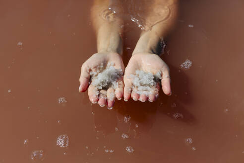 Hands of woman holding salt in lake - SIF00916