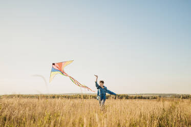 Happy boy running and flying kite in field - ANAF02151