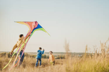 Father holding kite with sons in field under sky - ANAF02157