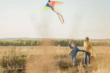Playful father and son flying kite in field - ANAF02159