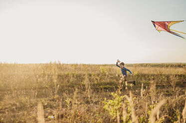 Happy boy running and flying kite in field under sky - ANAF02163