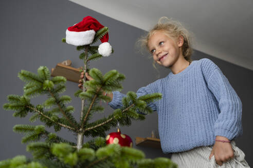 Lächelndes Mädchen beim Schmücken des Weihnachtsbaums zu Hause - SVKF01621